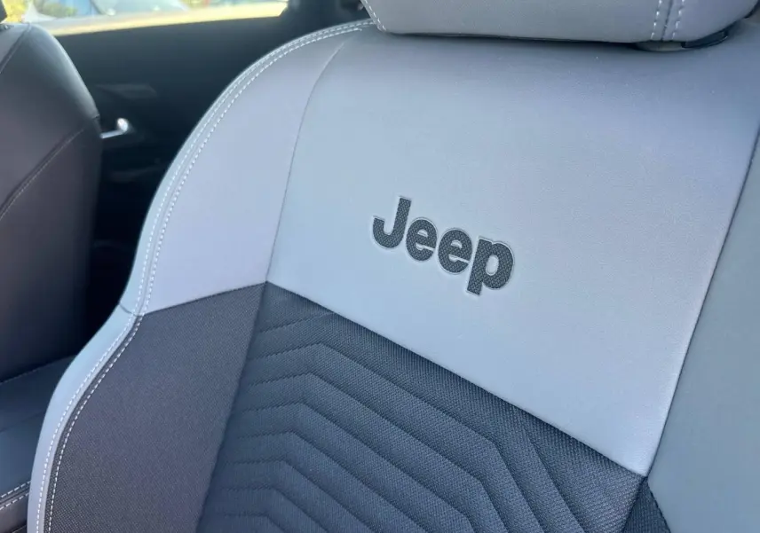 Gros plan sur le siège avant gris et noir du Jeep Compass 2026 avec logo Jeep brodé et surpiqûres blanches.