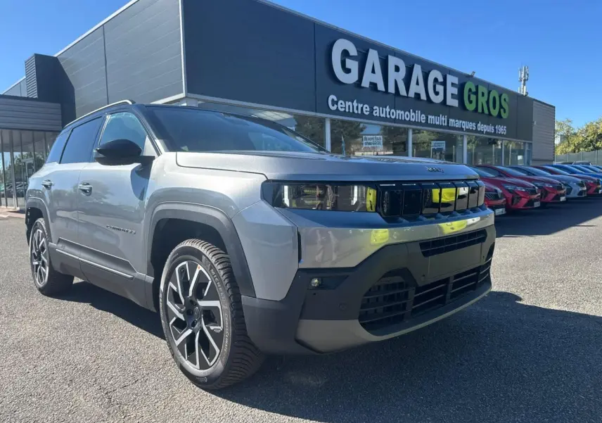 Jeep Compass Yosemite gris clair avec toit noir, vue 3/4 avant droit devant un garage automobile.