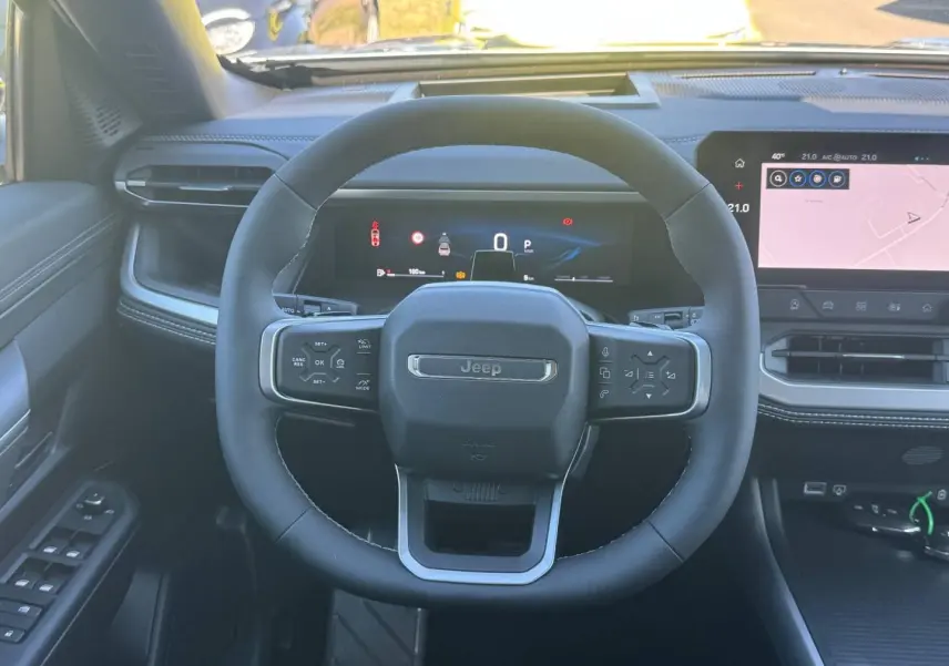 Vue intérieure centrée sur le volant Jeep noir avec tableau de bord digital et écran tactile à droite.