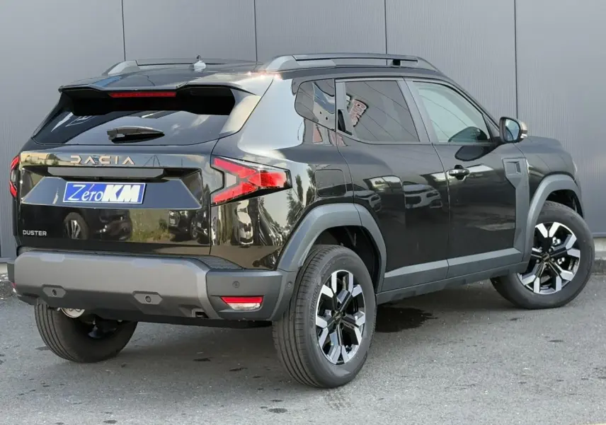 Vue 3/4 arrière droite du Dacia Duster noir nacré 2025 avec jantes alliage et barres de toit grises.