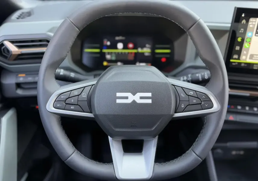 Volant noir du Dacia Duster 2025 avec commandes intégrées, tableau de bord digital et écran tactile visible en arrière-plan.
