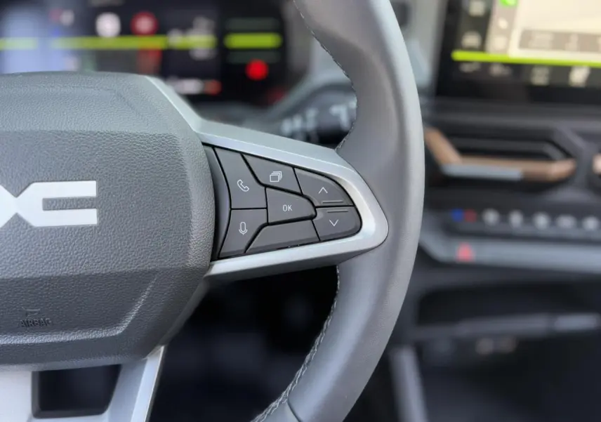 Gros plan sur le volant droit en cuir noir du Dacia Duster 2025 avec commandes intégrées et tableau de bord flou.