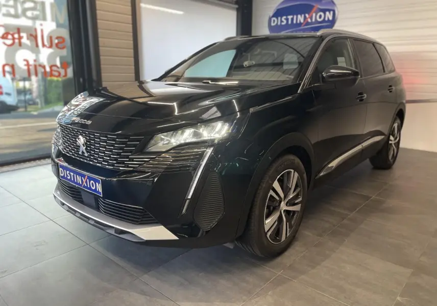 Peugeot 5008 noir métallisé vue 3/4 avant droit, avec calandre chromée et feux LED allumés en intérieur showroom.