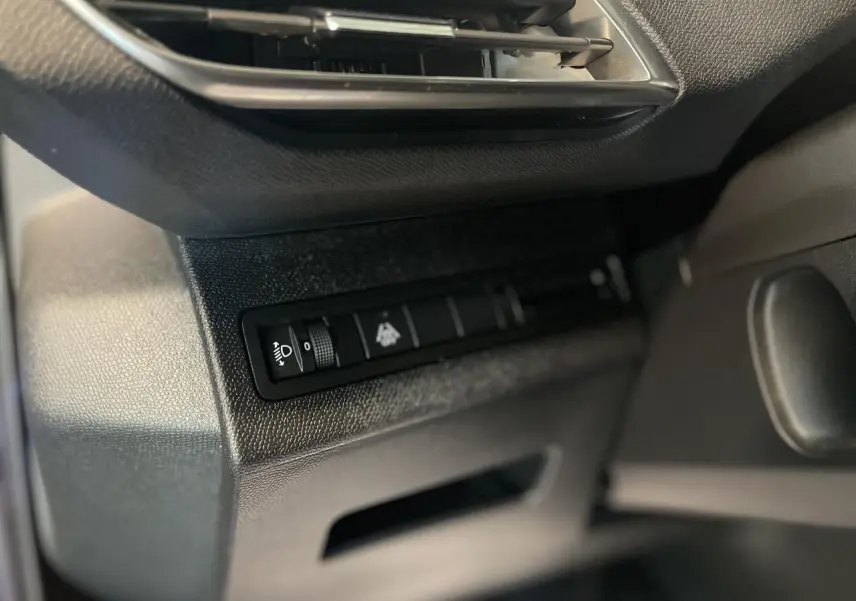 Détail du tableau de bord côté gauche du Peugeot 5008 2024 avec commande de réglage des phares et texture noire.
