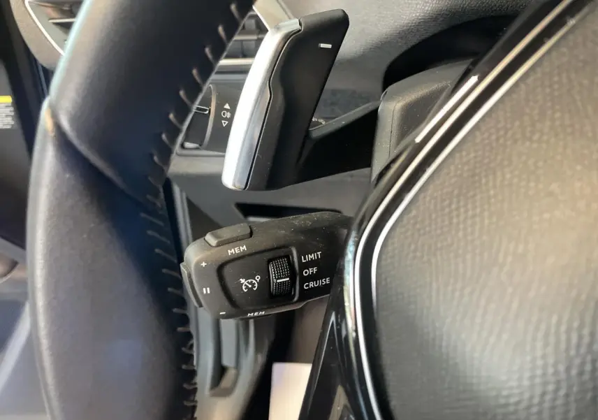 Gros plan sur la commande de régulateur de vitesse à gauche du volant noir du Peugeot 5008 2024 finition Allure Pack.