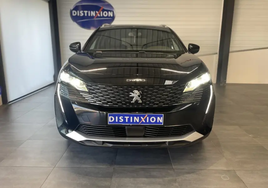 Vue frontale d'un Peugeot 5008 noir métallisé avec calandre à damier chromé et feux LED allumés en intérieur showroom.