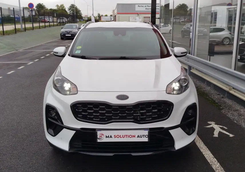Vue de face d'un KIA SPORTAGE blanc 2022 avec phares allumés et calandre noire distinctive.