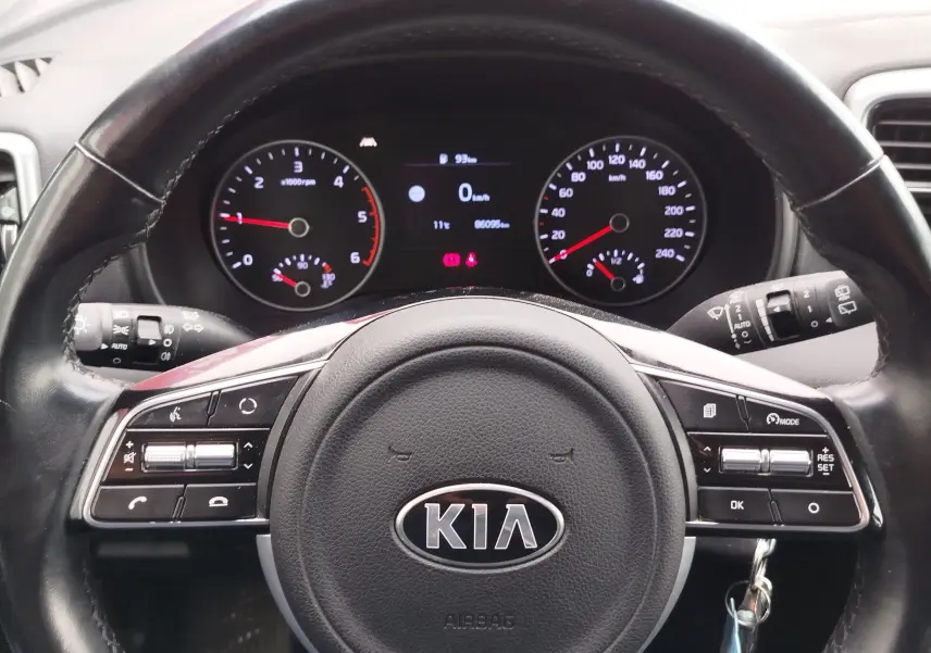 Vue rapprochée du volant noir KIA avec tableau de bord numérique affichant les compteurs et indicateurs du Sportage 2022.