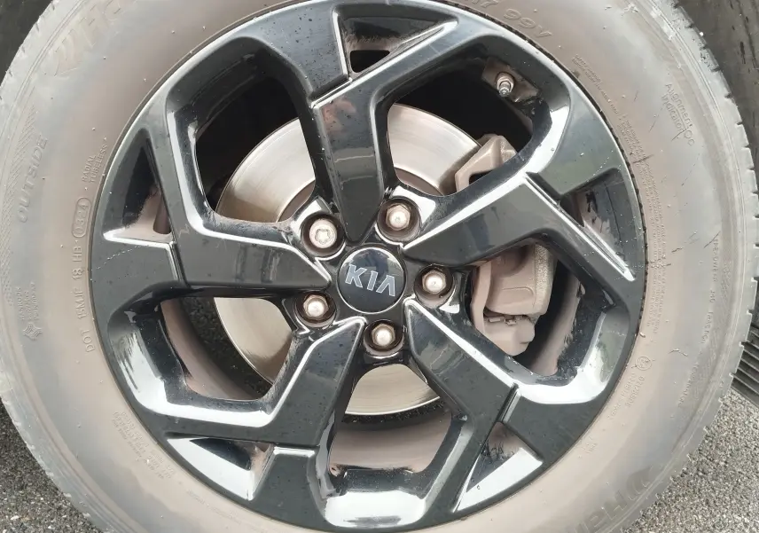 Gros plan sur la jante noire brillante d'un Kia Sportage blanc, mettant en valeur le logo central et le disque de frein.