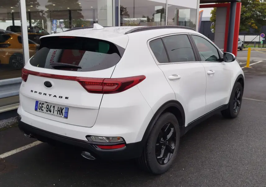 Vue 3/4 arrière droite d'un KIA Sportage blanc 2022 avec jantes noires et feux arrière allongés.