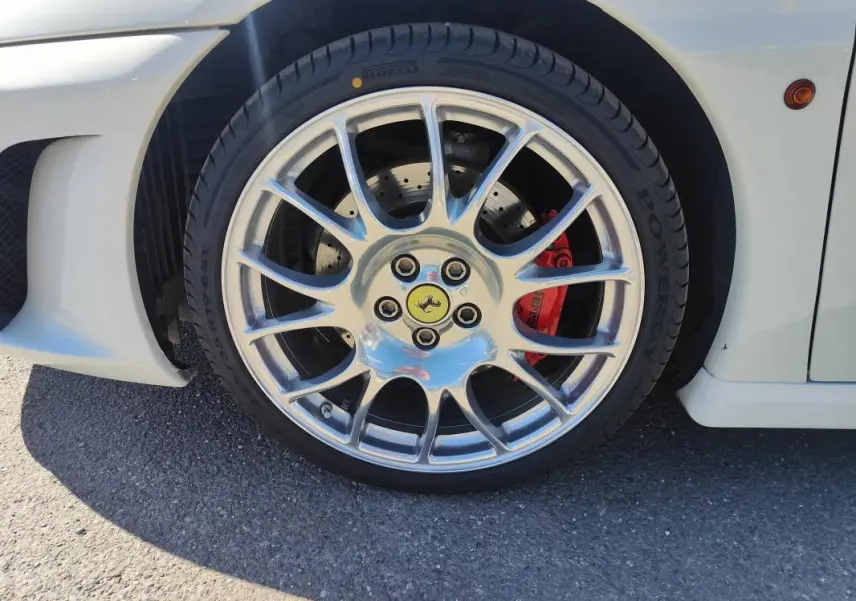 Gros plan sur la roue avant droite d'une Ferrari F430 Spider blanche, avec étrier de frein rouge et jante argentée brillante.