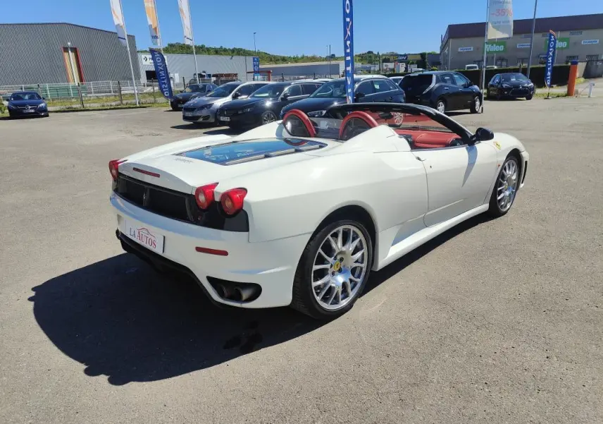 Ferrari F430 Spider blanc vue 3/4 arrière droit, capote ouverte et intérieur cuir rouge visible.