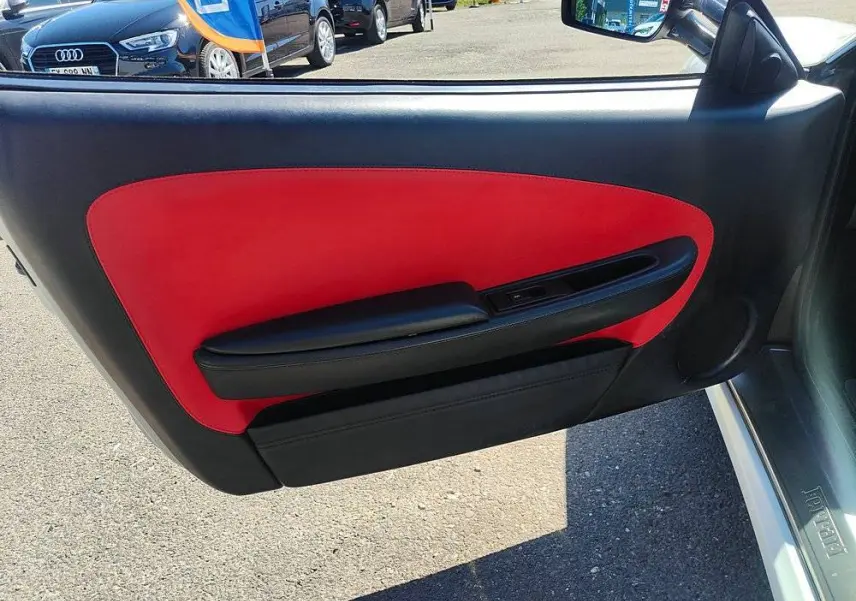 Intérieur de la porte côté gauche d'une Ferrari F430 Spider blanche, avec garniture rouge et noire visible.