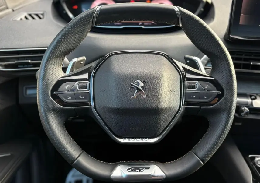 Volant cuir perforé Peugeot 3008 GT vu de face avec badge GT et commandes multifonctions intégrées.