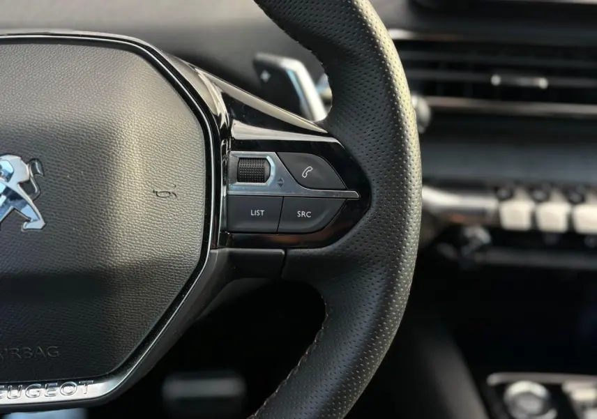Gros plan sur le volant cuir perforé à droite du Peugeot 3008 2023, avec commandes intégrées et finition noire brillante.