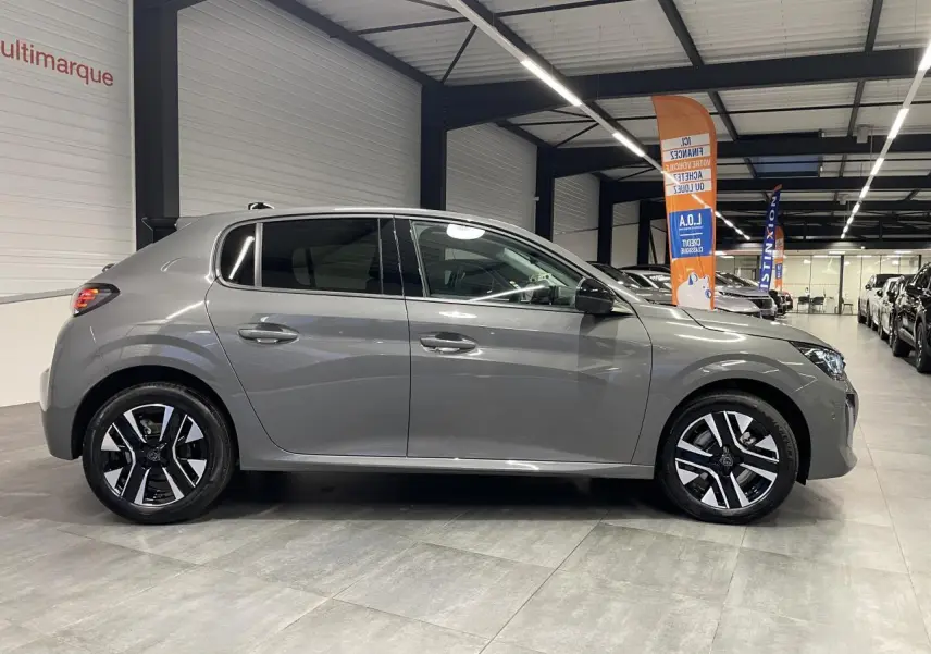 Peugeot 208 gris sélénium vue de profil côté gauche en intérieur avec jantes alliage bi-tons et rétroviseurs noirs.