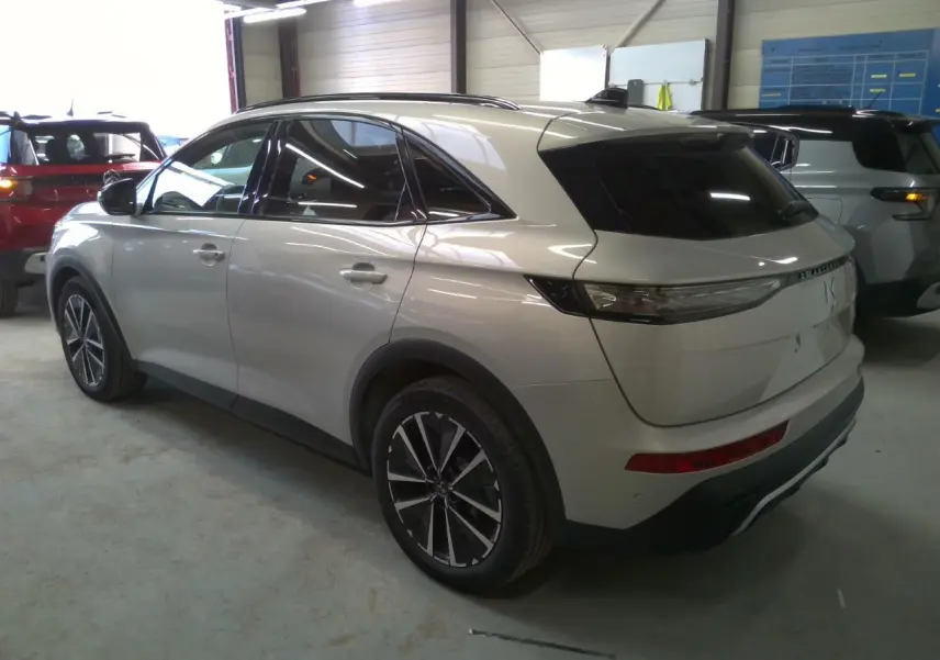 Vue 3/4 arrière droite d'un DS7 Cristal Pearl avec jantes alliage et barres de toit noir brillant en intérieur garage.