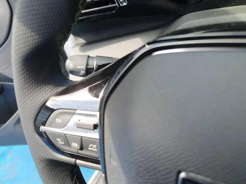 Gros plan sur le volant multifonction noir de la Peugeot 308 Hybrid, avec commandes intégrées et finition brillante.