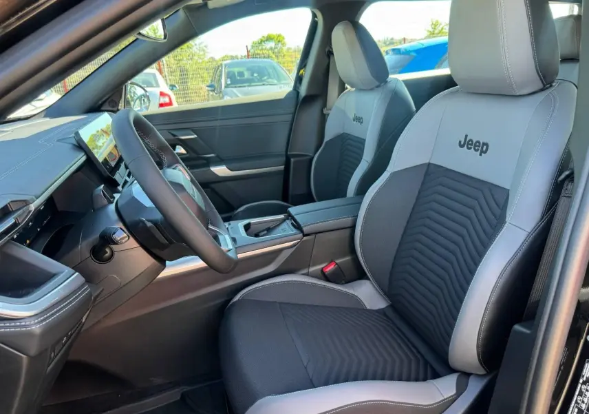 Vue intérieure côté conducteur du Jeep Compass 2026, sièges tissu gris/anthracite avec logo Jeep brodé.