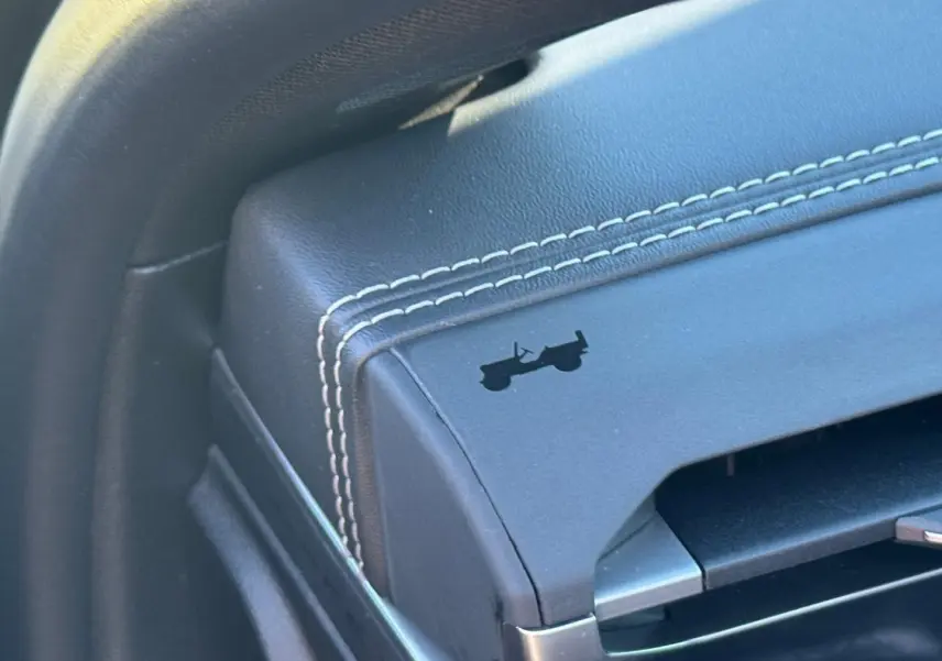 Détail de l'accoudoir central en cuir noir avec surpiqûres blanches et logo Jeep en relief.