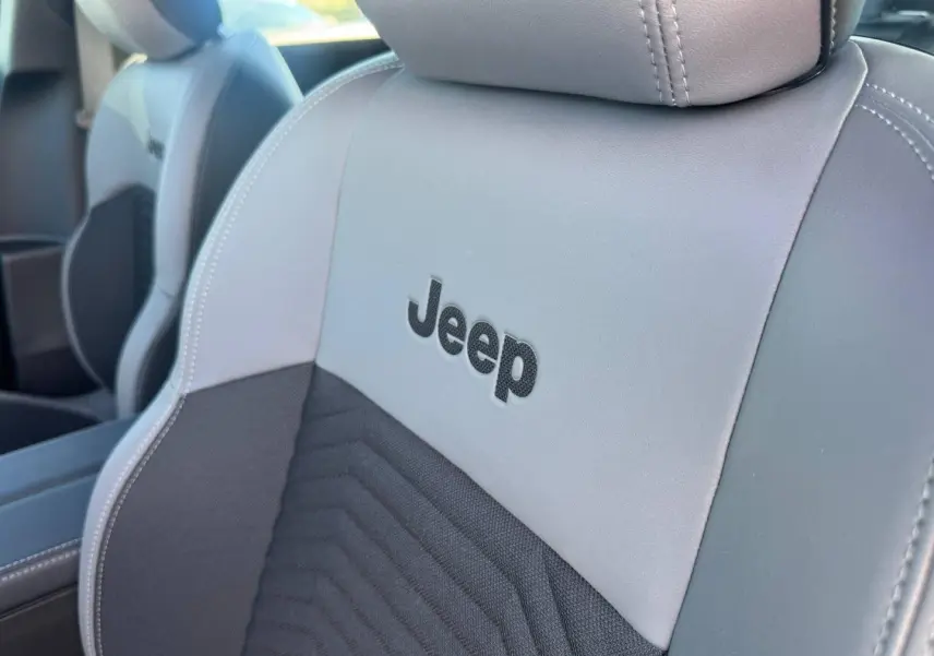 Gros plan sur le siège avant gris et anthracite avec logo Jeep brodé, montrant les détails de couture et texture du tissu.