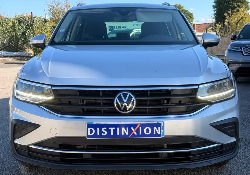 Vue de face d'un Volkswagen Tiguan 1.5 TSI 150CH LIFE DSG7 en reflet argent avec calandre noire et phares LED allumés.