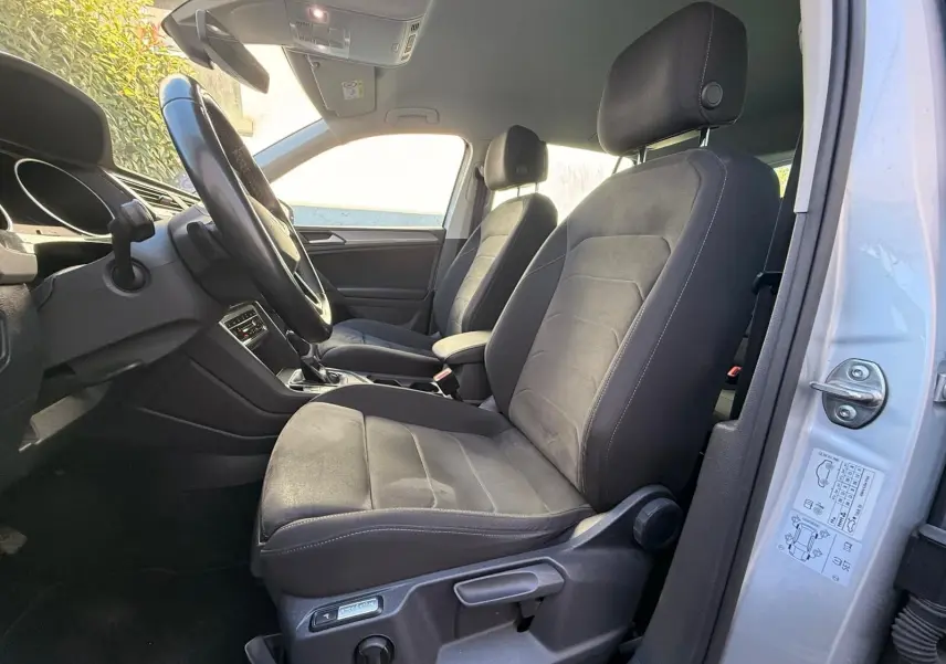 Vue intérieure côté conducteur du Volkswagen Tiguan 2021 avec sièges Ergo Active en tissu noir et portière argentée ouverte.