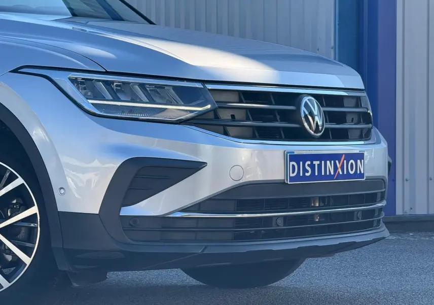 Vue 3/4 avant gauche d'un Volkswagen Tiguan 2021 couleur reflet argent avec calandre noire et logo VW visible.