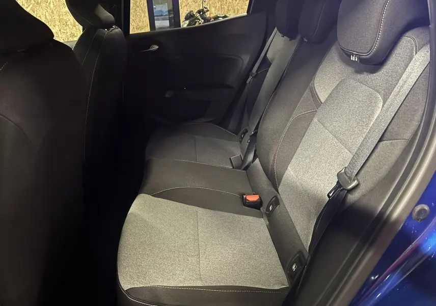 Vue intérieure côté droit des sièges arrière en tissu gris et noir d'une Renault Clio 2024 bleu Iron avec ceinture de sécurité visible.