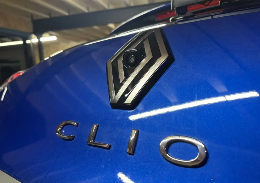 Gros plan sur le logo Renault avec caméra intégrée et l'inscription Clio sur la malle arrière bleu iron d'une Clio 2024.