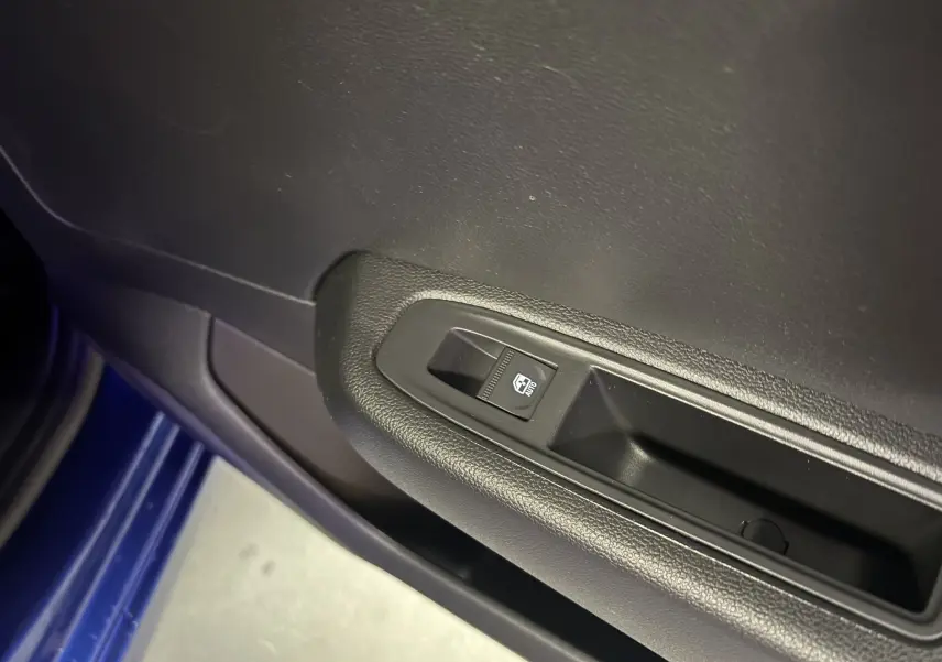 Gros plan sur la commande de lève-vitre côté conducteur dans la porte noire d'une Renault Clio bleu iron 2024.