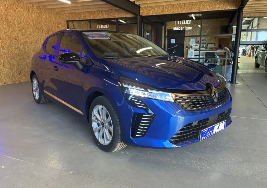 Renault Clio TCe 90ch X-Tronic Evolution bleu Iron en 3/4 avant droit, avec phares LED allumés dans un atelier.