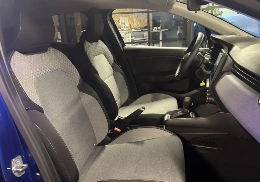 Intérieur de la Renault Clio TCE 90CH X-TRONIC Evolution 2024, vue côté gauche sur sièges tissu gris et tableau de bord noir.