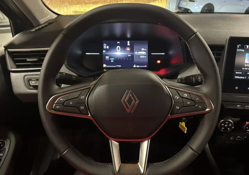 Vue rapprochée du volant noir de la Renault Clio 2024 avec commandes intégrées et tableau de bord digital allumé.