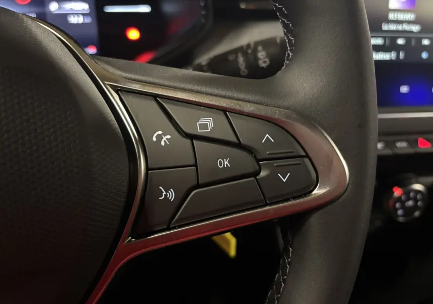 Gros plan sur les commandes au volant côté droit de la Renault Clio 2024 bleu iron, avec boutons multifonctions et finition noire.