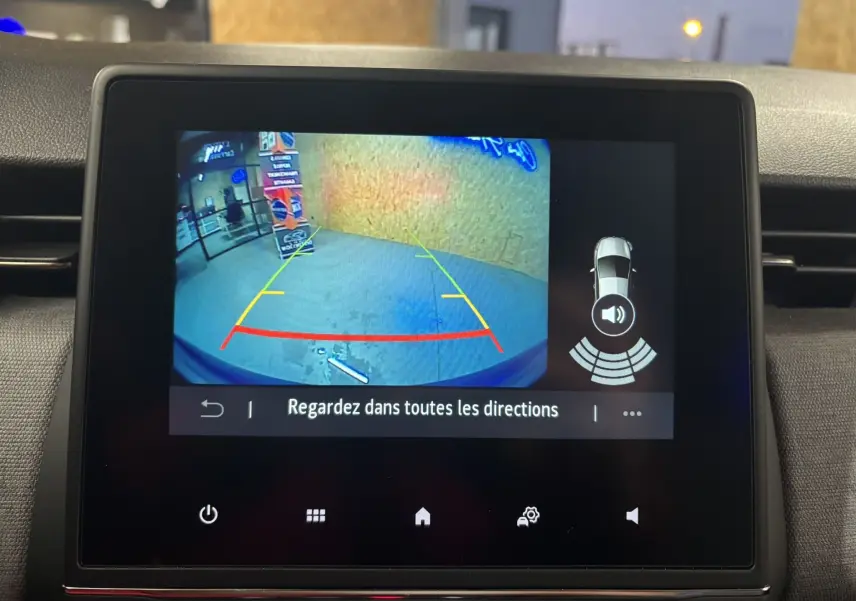 Écran multimédia montrant la caméra de recul d'une Renault Clio bleu Iron avec lignes d'aide au stationnement.