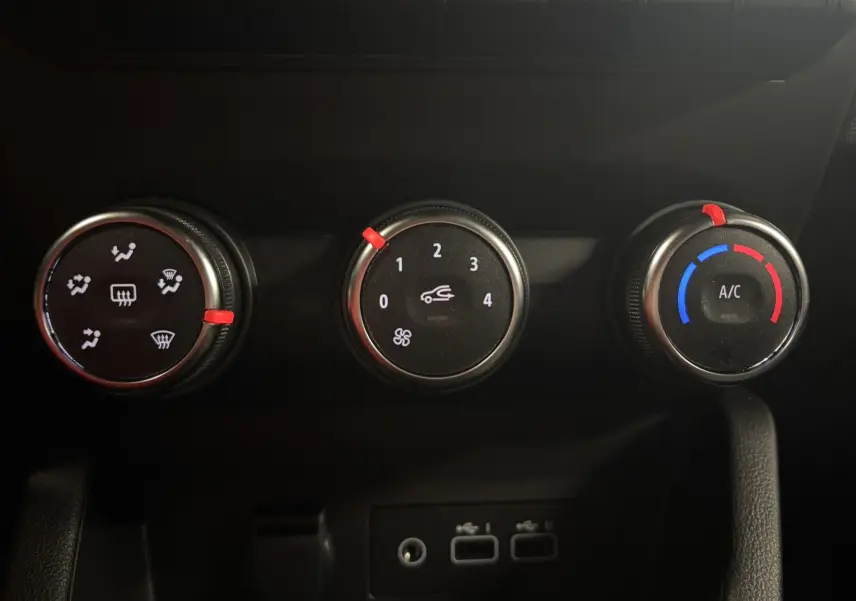 Commandes de climatisation avec trois molettes noires et détails rouges à l'intérieur d'une Renault Clio bleu Iron 2024.