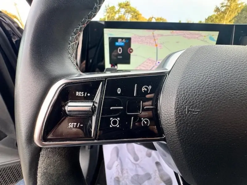 Gros plan sur les commandes de régulateur de vitesse au volant du Renault Espace hybride 2023 avec écran GPS en arrière-plan.