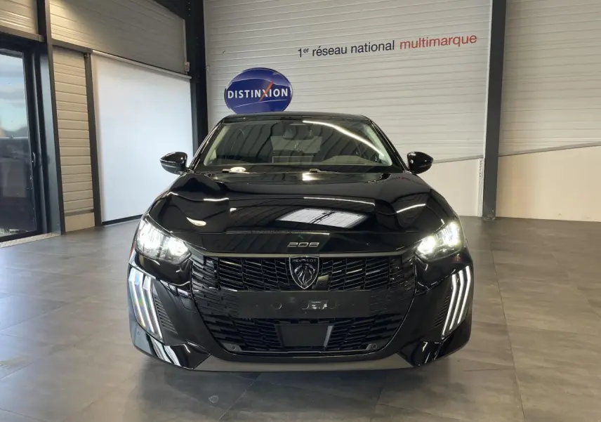 Vue avant d'une Peugeot 208 noire 2025 avec phares allumés et calandre noire brillante en intérieur showroom.
