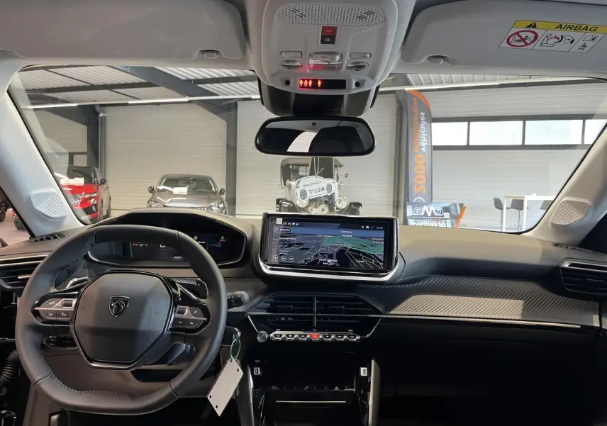 Vue intérieure avant du Peugeot 208 noir hybride 2025, mettant en valeur le tableau de bord avec écran tactile et volant compact cuir.