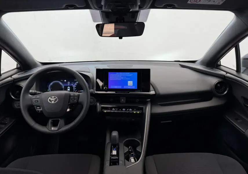 Vue intérieure avant du tableau de bord noir du Toyota C-HR 1.8 Hybride 2024 avec écran tactile central allumé.