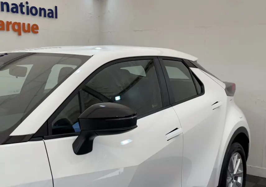 Vue côté gauche avant d'un Toyota C-HR 1.8 Hybride blanc avec rétroviseur noir et poignées de porte intégrées.