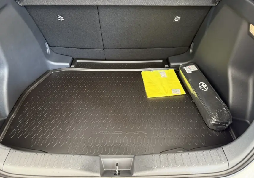 Coffre ouvert du Toyota C-HR blanc 2024, vue arrière, avec tapis de coffre noir marqué C-HR et accessoires rangés.