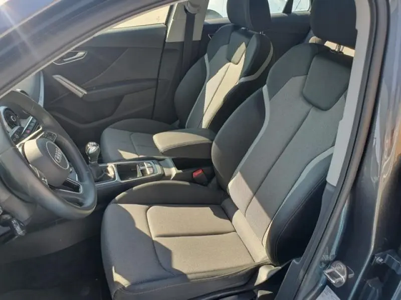 Vue intérieure côté gauche de l'Audi Q2 30 TDI 116ch Design 2025 avec sièges sport tissu gris et volant cuir multifonction.