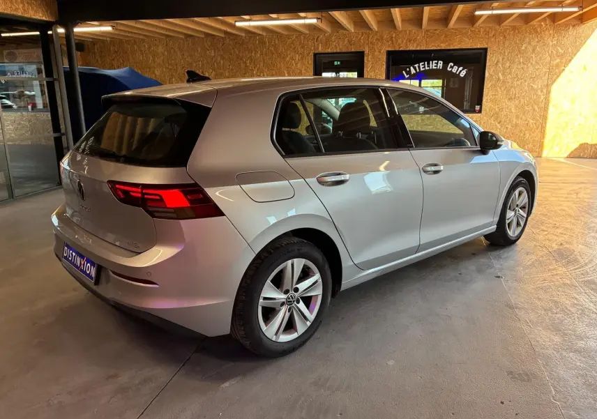 Volkswagen Golf 1.0 eTSI 110 DSG7 gris clair vue 3/4 arrière droit en intérieur avec feux arrière allumés.