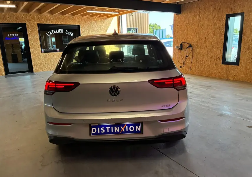 Vue arrière d'une Volkswagen Golf gris clair 2023 avec feux LED allumés, stationnée dans un garage lumineux.