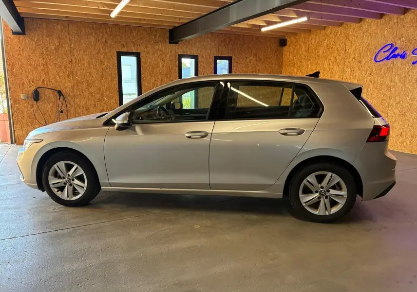 Vue de profil côté gauche d'une Volkswagen Golf gris clair 2023, version 1.0 eTSI 110 DSG7 LIFE PLUS, en intérieur.