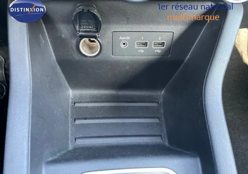 Vue rapprochée de la console centrale noire avec prise 12V, ports USB et entrée Aux-In d'une Renault Clio Société blanche.