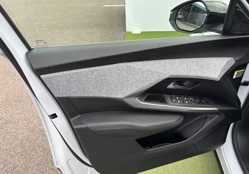 Porte avant gauche ouverte d'un Peugeot 3008 blanc Okenite, montrant le panneau avec commandes et décor tissu gris chiné.