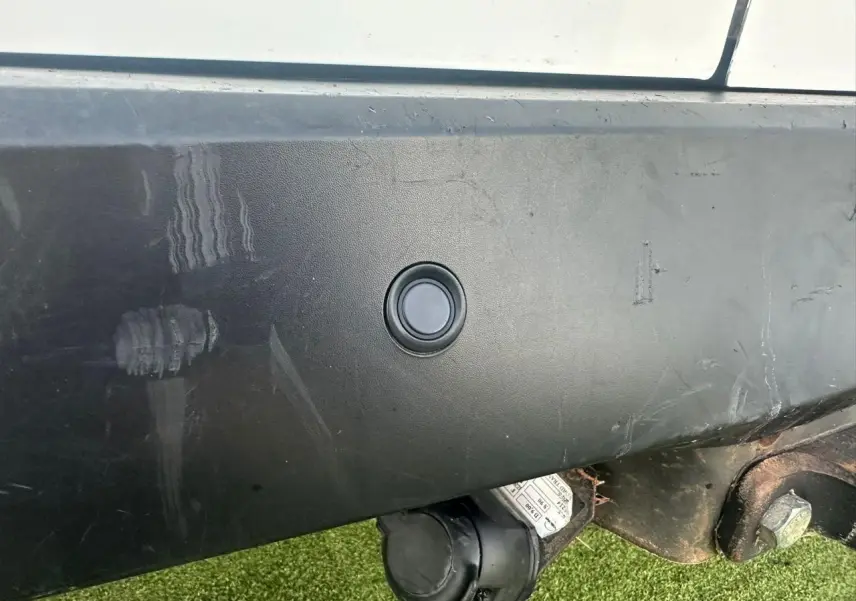 Gros plan sur le pare-chocs arrière noir du Ford Transit Connect blanc, avec prise de remorquage visible en bas à droite.